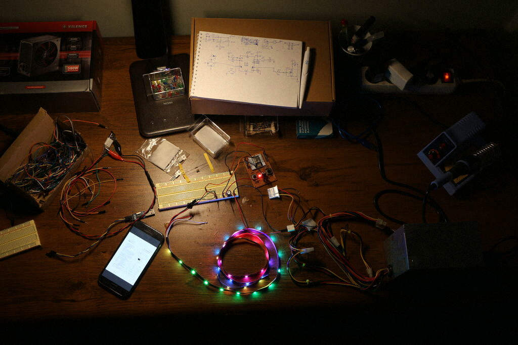 A messy desk with LED strip, wires, breadboard and other parts on it. A mobile phone is on displaying data sheet for some electronics